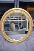A 20th-century large oval ornate mirror, having a gilt-frame of repeating leaf design, two wall
