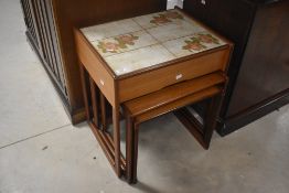 A vintage teak nest of three tables, the top table having frieze drawer and foliate tile top,