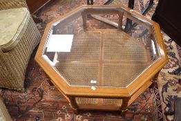 A modern coffee table of octagonal form having glass top and canework undertier, width approx. 95cm