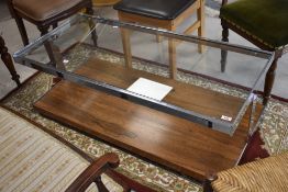 A vintage glass topped coffee table having chrome frame and laminate wood effect undertier, on
