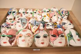 A selection of forty ceramic face masks, varied in size and decoration.