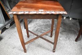 A mahogany style stained side table having scalloped top edge and cross bracers measuring 63cm