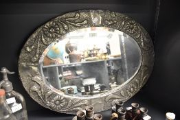 An Arts & Crafts pewter mounted and bevelled wall mirror, of oval form hand embossed with stylised