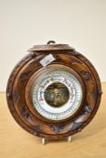 A small 20th century circular barometer, with partially exposed mechanism and carved walnut