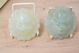 Two 20th-century Chinese carved green-stone pendants, possibly jade, depicting a foo dog-like