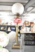 A large vintage oil lamp raised on a two-step brass pedestal and column, having rich pink oil font