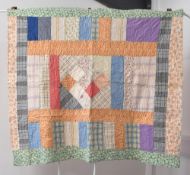 An antique 20th century handmade patchwork cot quilt, having a central grid and border in vibrant