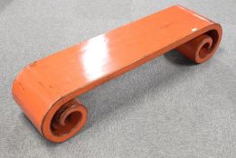 An attractive Chinese red-lacquered scroll end bench or low table, of oblong form with pronounced
