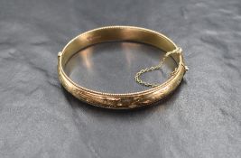 A 9ct gold hinged bangle, the bangle having decorative scroll engraving with twisted rope motif