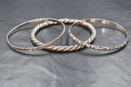 A trio of white metal slave bangles, the two slim moulded bangles being stamped sterling and