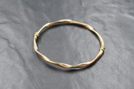 A 9ct gold hinge bangle, of twisted form with a safety catch, marked 9kt, 6.5cm diameter, 4.1g