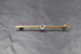 A yellow metal bar brooch marked 15, having a central claw set blue topaz, approx 3g gross