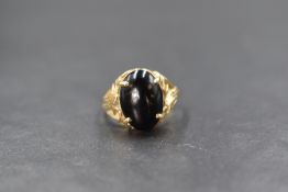 A yellow metal presumed gold black stone set ring, the central oval black cabochon in an ornate