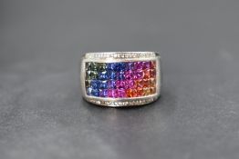 A silver band ring of broad form having an inset panel of 36 rainbow sapphires bordered by diamond