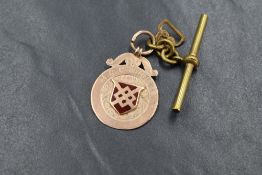 A 9ct rose gold medalion having enamelled decoration to front and a monogram en verso, on a rolled