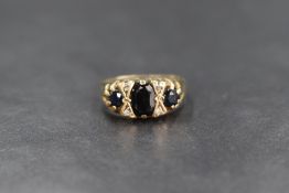 A 9ct gold sapphire and diamond set ring, the central oval cut sapphire flanked by a round cut
