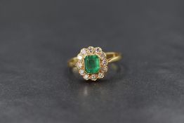 An 18ct gold emerald and diamond set cluster ring, the central emerald cut emerald in a bezel