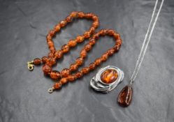 A modern silver amber set brooch, the oval amber cabochon within in a fluid ribbon motif closed back