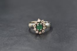 A white metal emerald and diamond cluster ring stamped 18ct having an oval emerald, approx 0.5ct