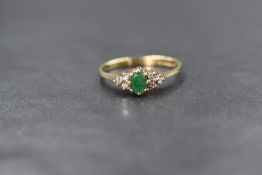 A 9ct gold emerald and diamond set ring, the central oval cut emerald flanked by three round cut