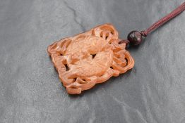 A Chinese carved orange jade style pendant depicting two fish within water, with a wooden bead on