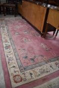 A large Chinese pink ground rug/carpet of traditional design with fringed ends 274cm x 182cm