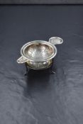A George V silver tea strainer, of traditional form with moulded rim, on a silver wire stand,