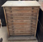 A pine collectors cabinet with a rectangular top above ten drawers on a plinth base