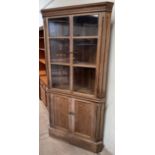 An oak corner cupboard with a moulded cornice and glazed doors,