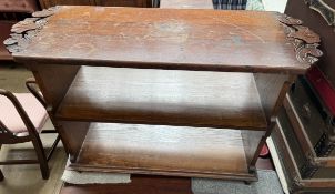 An oak bookcase, the top shelf with carved ends above two other shelves on casters,