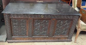A 17th century carved oak coffer with a planked top above a three panel front on stiles