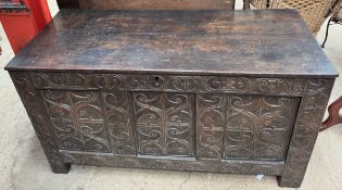 An oak coffer with a planked rectangular top above a carved three panel front on stiles,