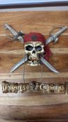 Wall-mounted resin skull with red bandana, crossed sabres and suspended “Pirates of the