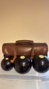 Three lawn bowls with leather carry case