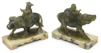 A pair of Chinese carved green hardstone figures of boys riding buffaloes