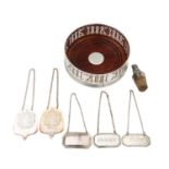 A group of five silver decanter labels, a Millennium coaster and a Peruvian silver mounted cork