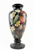 LATE VICTORIAN BLACK PAINTED CERAMIC FOOTED VASE WITH FLORAL DISPLAY