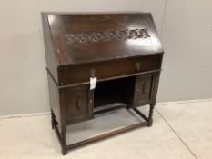 A dark oak Tudor style bureau with a decorative carved front, single drawer above cupboard doors,