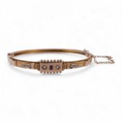 An Edwardian 9ct, seed pearl and ruby set hinged bangle, interior diameter 57mm, gross weight 8.3 gr