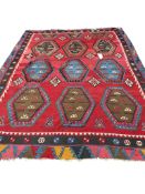 A Turkish Kilim flatweave polychrome carpet, woven with three rows of hexagons, on a red ground, (