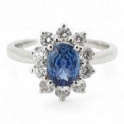 A sapphire and diamond cluster ring, claw-set with an oval sapphire weighing approximately 0.77