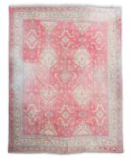 A large Turkish faded red ground carpet woven with rows of geometric lozenge medallions within a