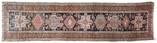 An early 20th century Caucasian dark blue ground runner woven with a row of geometric and lozenge