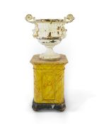 A Victorian white painted cast iron urn and a painted faux marble pedestal, the twin handled urn