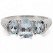 A modern 10k white metal and three stone oval cut aquamarine ring, with six stone diamond chip set