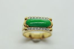 AN 18CT YELLOW GOLD RING SET WITH PILL SHAPED JADE PANEL FLANKED BY FOURTEEN SMALL DIAMONDS.
