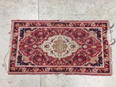 A HAND CRAFTED RUG ON A RED GROUND - REQUIRES ATTENTION W 90 X H 170CM.