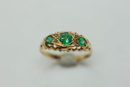 AN EMERALD RING, THE THREE STONES DIVIDED BY TINY DIAMONDS, ON AN 18CT GOLD BAND.