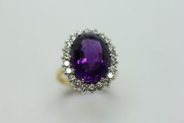 AN AMETHYST AND DIAMOND RING, THE CENTRAL OVAL STONE SURROUNDED BY SMALL BRILLIANT CUT DIAMONDS,