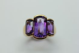 A THREE STONE AMETHYST RING ON A 9CT GOLD BAND.